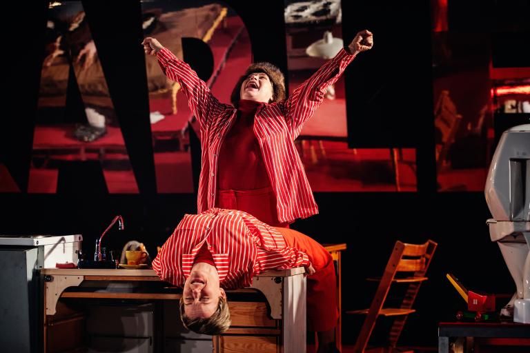 En person ligger bakåtlutad över en köksbänk medan en annan person står bakom med armarna lyfta.