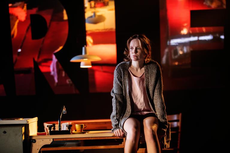 En person sitter på en köksbänk och tittar bortåt under varm belysning.