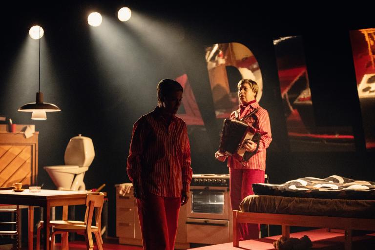 Två personer står i köksinteriör, en av dem håller ett dragspel.