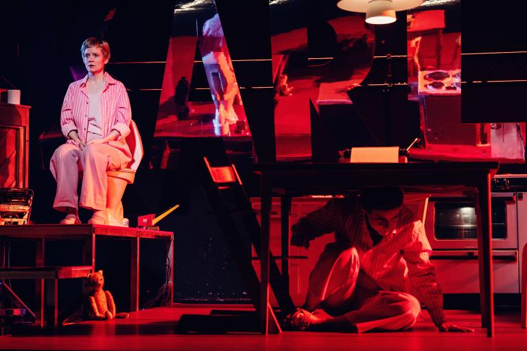 Person sitter på en toalettstol på en plattform medan en annan kryper fram under ett bord.