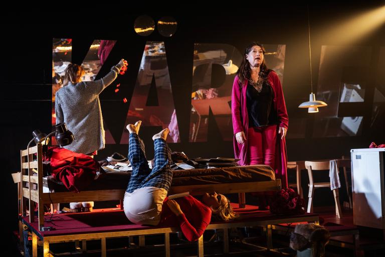 En person står och sjunger och två rullar runt och böjer sig i en säng