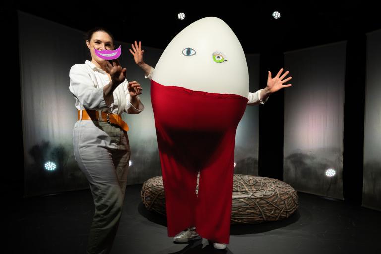 En skådespelare står bredvid en annan utklädd till ett stort ägg med ögon i papper. Ägget bär röda byxor och sträcker ut armarna.
