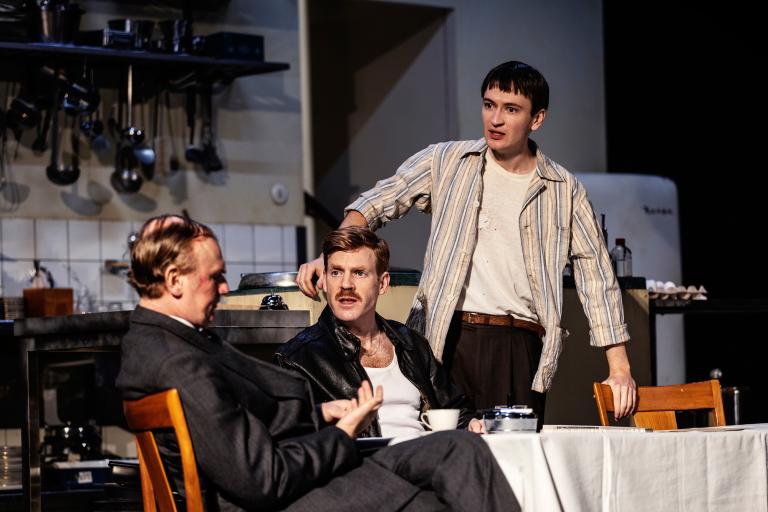 Tre personer runt ett matbord. En står upp.