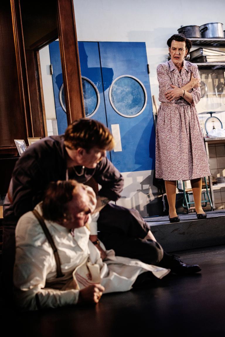 Två personer slåss på golvet. En person i bakgrunden.