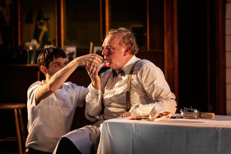 En person vid ett bord får hjälp av en annan att lyfta sitt vattenglas.