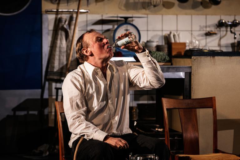 En person i vit skjorta sitter ner och halsar ur en flaska.