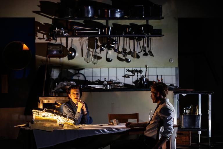 Två personer vid ett matbord. En kristallkrona ligger på bordet och lyser upp.