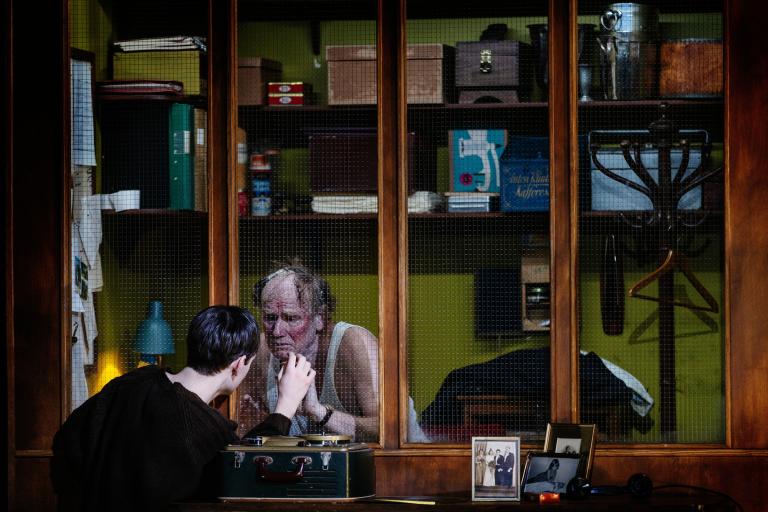 En person vid en fönsterruta i ett kontor. En annan person håller sin hans mot rutan på andra sidan.