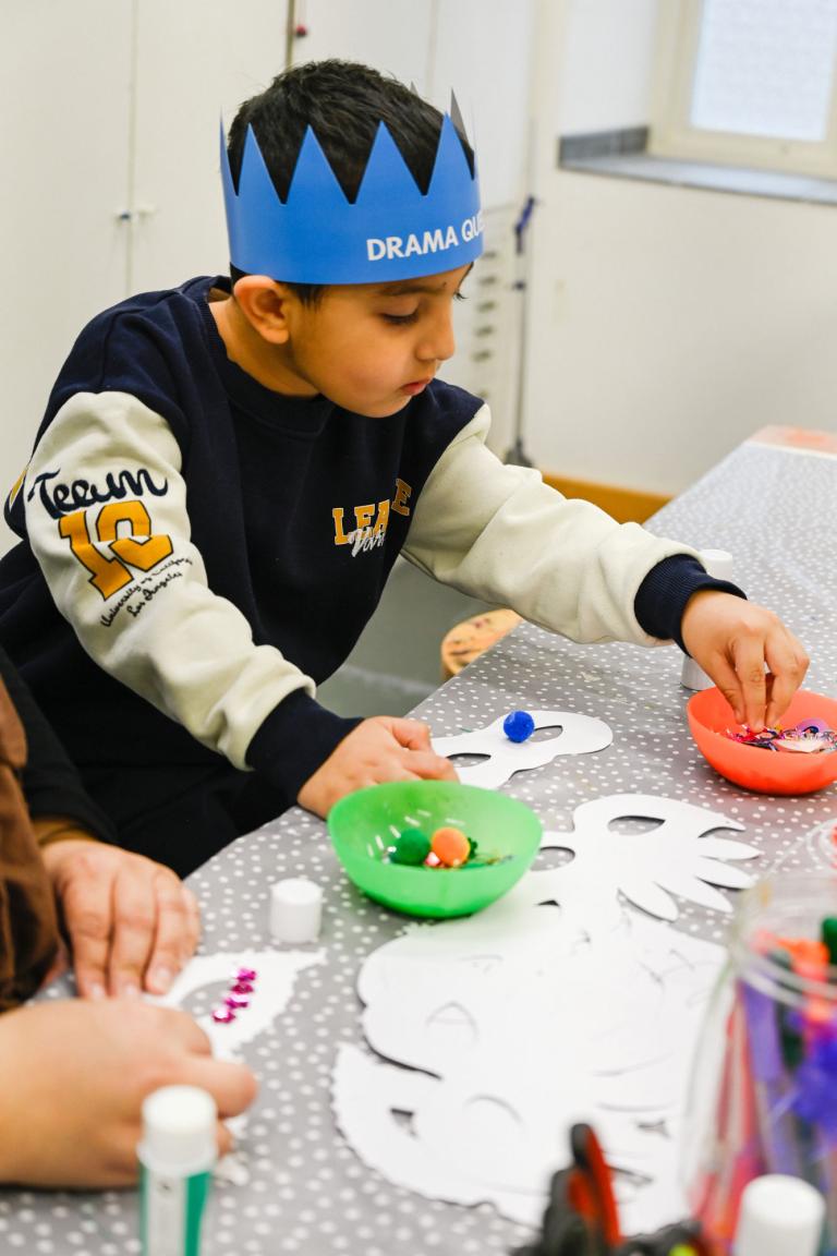 barn i pappkrona sitter vid bord och pysslar en teatermask
