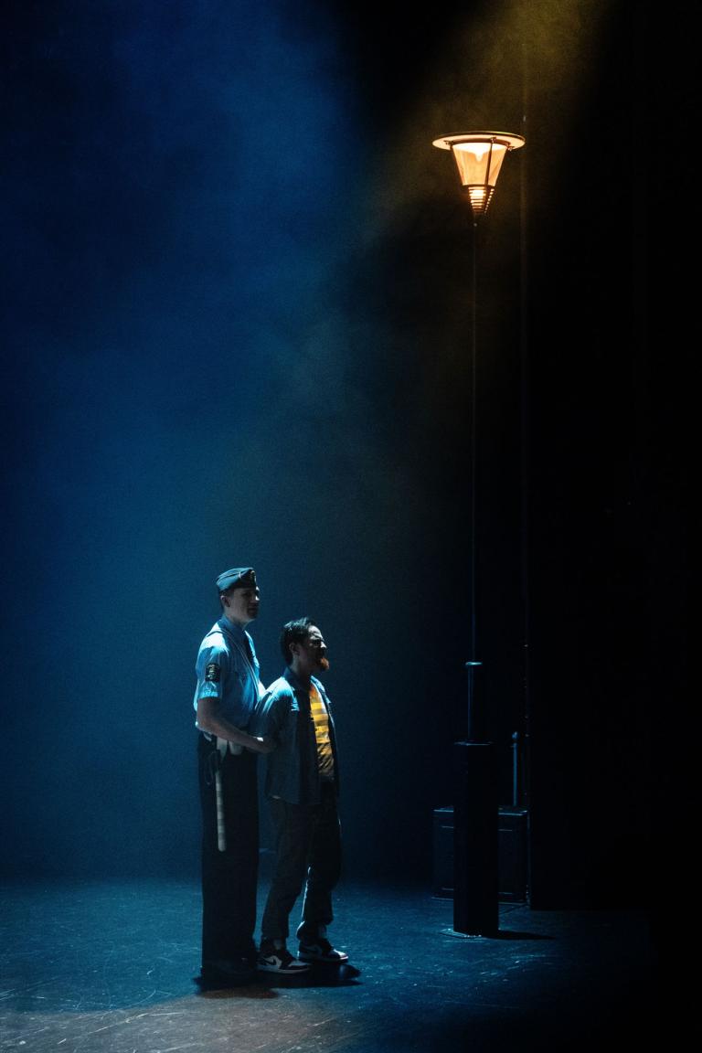 Polis håller en man i armen under en gatlykta i blått scenljus.