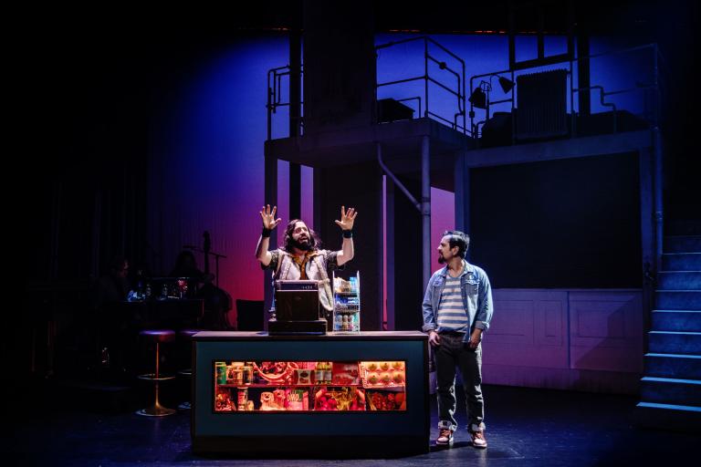 Två skådespelare står vid en butiksdisk på scenen.