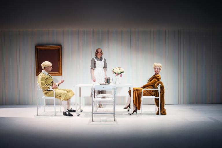 Tre personer vid ett vitt bord; en sitter mittemot en leende kvinna medan en tredje står bakom.