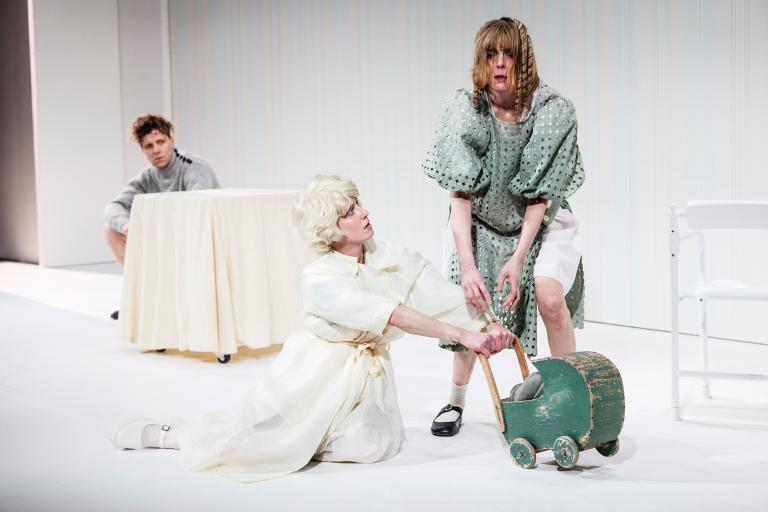 Två kvinnor vid en barnvagn; en står stelt medan den andra sitter på knä och håller i vagnen.