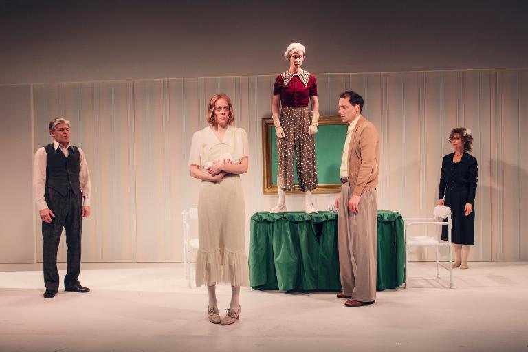 Fem personer på scen; en kvinna står på ett bord medan de andra står runtomkring.