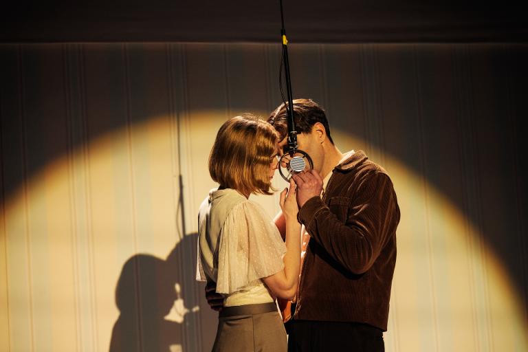 Två personer står nära varandra vid en hängande mikrofon, pannorna nästan mot varandra.
