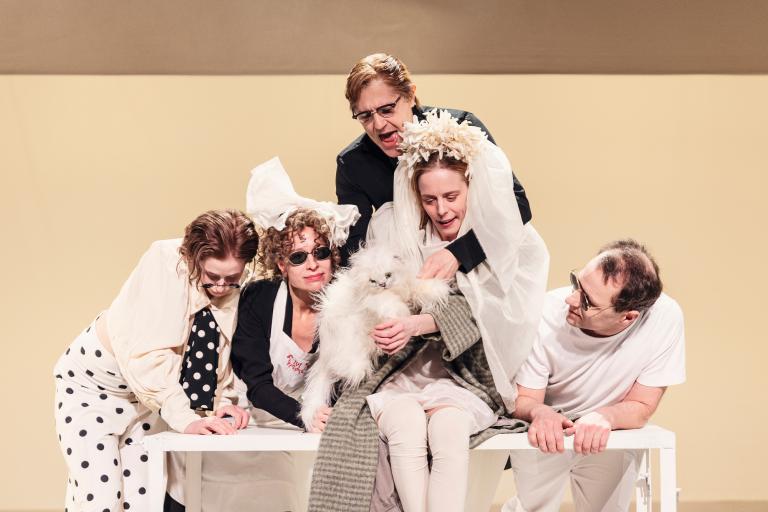 Fem personer samlade kring en kvinna som håller en vit katt; de lutar sig in mot henne.