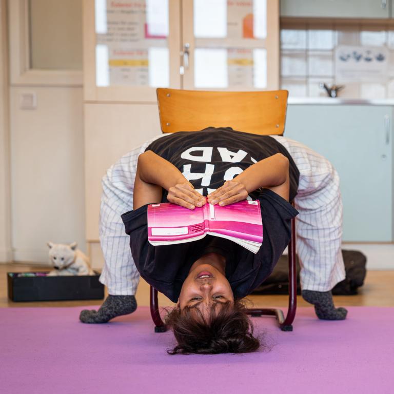 en skådespelare sitter baklänges upp och ned på en stol och läser ett anteckningsblock