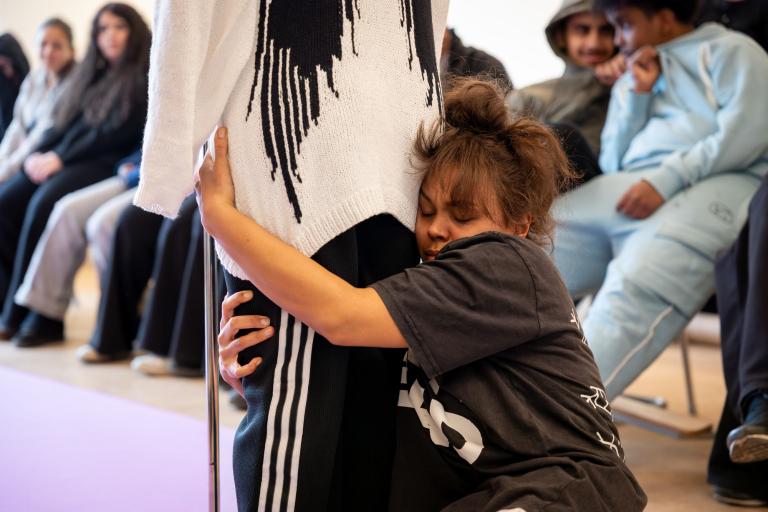 en skådespelare i svart tshirt kramar krampaktigt om en annan skådespelares ben