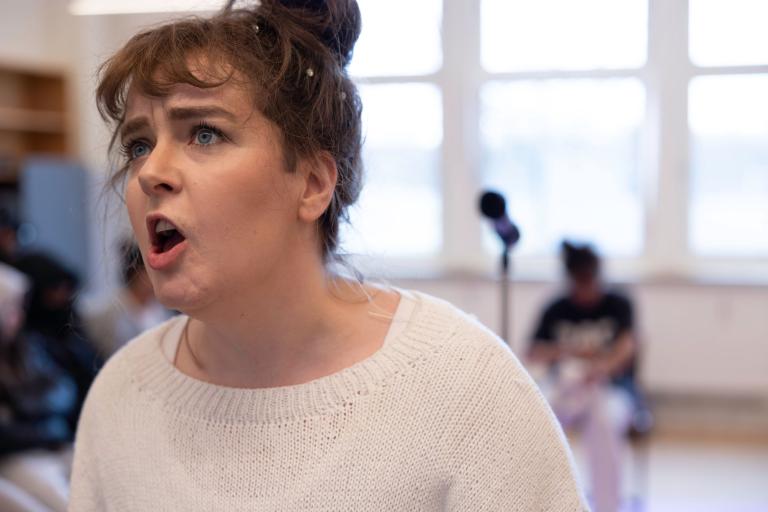 en skådespelare i vit tröja skriker mot något i fjärran. 