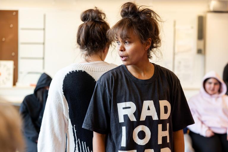 två skådespelare står rygg mot rygg och i bakgrunden syns publik