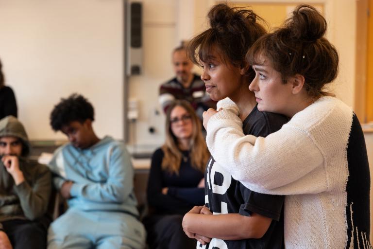 en skådespelare håller om en annan bakifrån