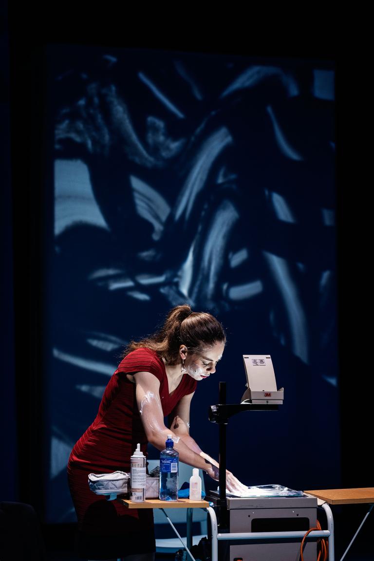 Skådespelare i röd klänning arbetar vid overheadapparat.