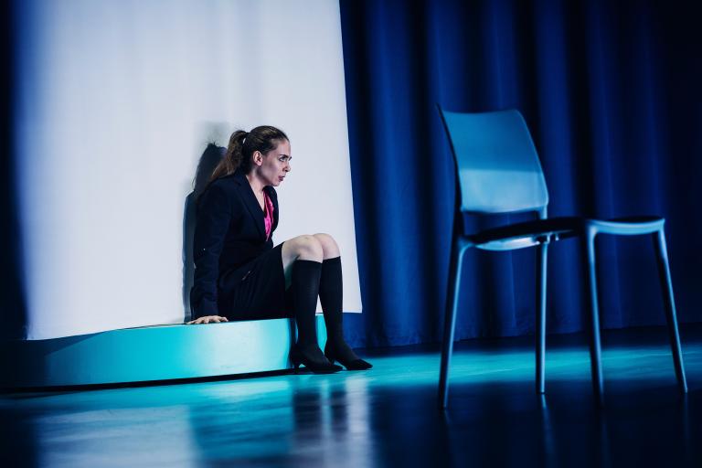 Skådespelare sitter vid scenkant bredvid stol.