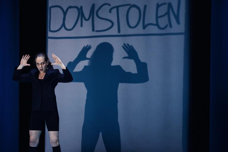 Skådespelare står i ljus framför projektion med text.