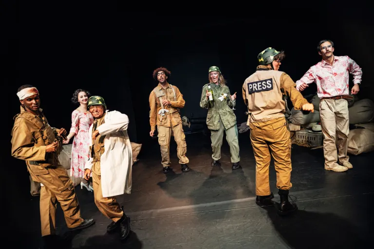 Ensemble i militärkläder och civila kläder utspridd på scen i en dramatisk scenbild.
