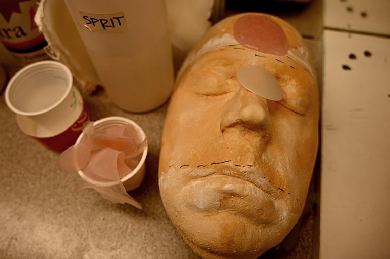 Ett ansikte i gips ligger på ett arbetsbord. Ovanpå ett antal färgprover i olika hudtoner.
