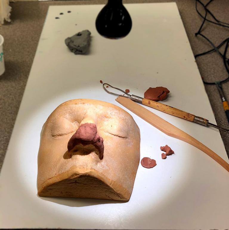 Gipsavgjutning av ansikte med lera på näsan och olika verktyg.