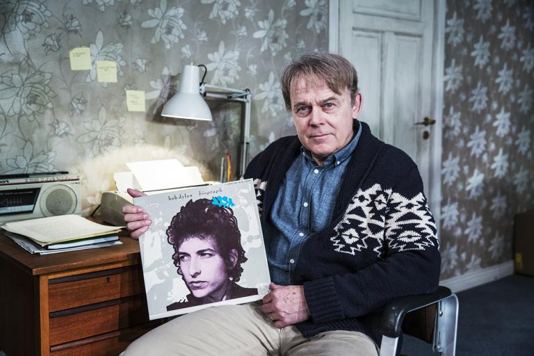Markus sitter vid sitt skrivbord och håller upp Bob Dylans samlingsalbum Biograph
