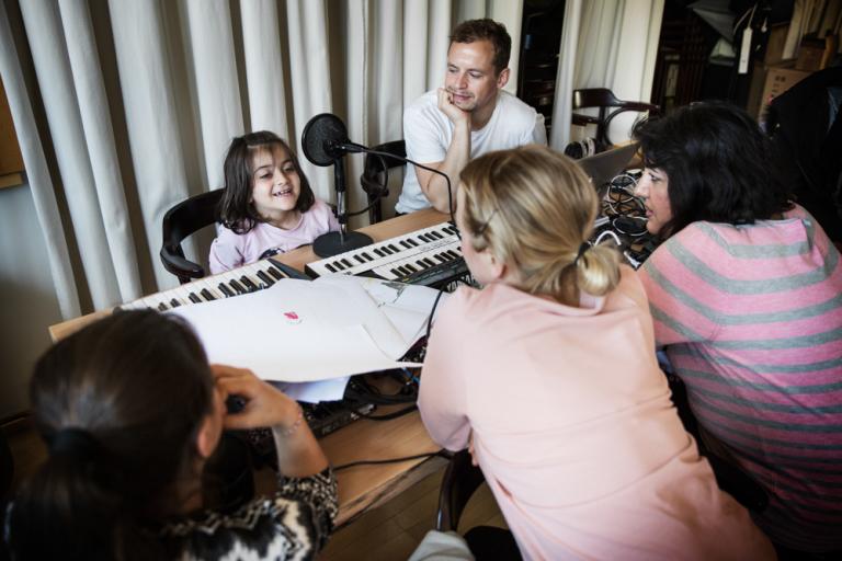 En flicka sitter vid ett keyboard och en mikrofon och bredvid sitter en vuxen och ler.