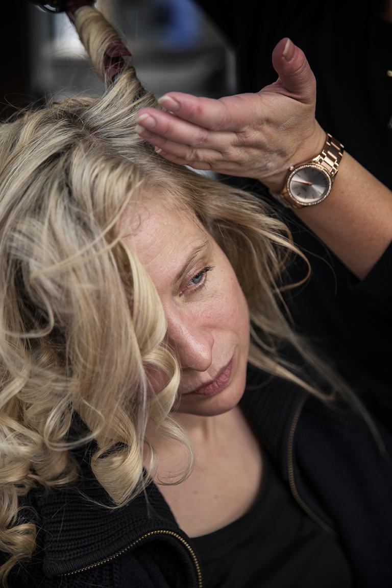 Närbild på en kvinnas ansikte vars hår lockas med locktång av en annan person.