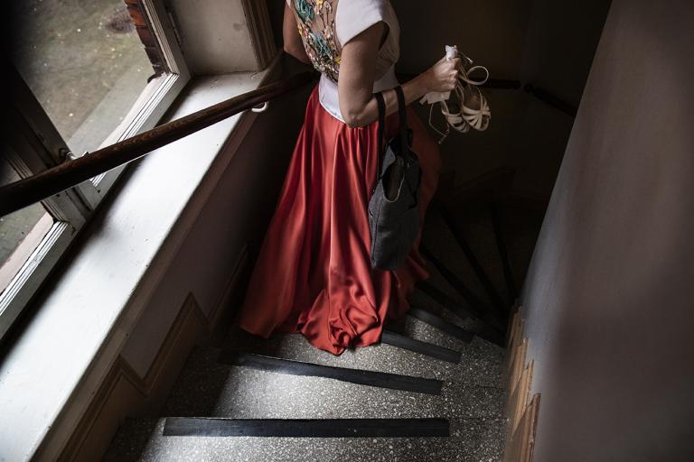 Kvinna med röd kjol och vit blus med broderade blommor på ryggen går ner för en trappa.