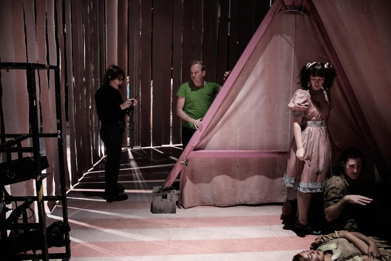 Två personer står bredvid ett rosa tält och i tältet gömmer sig skådespelare i kostymer