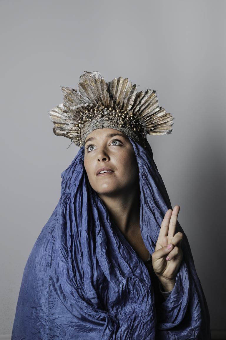 Kvinna klädd i blå sidentyg runt huvudet och med en silvrig krona har en from uppsyn