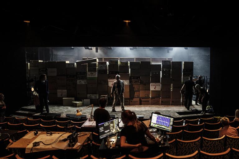 En man står på en teaterscen och repeterar. Scenen består av en vägg gjord av flyttkartonger. 