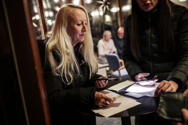 Kvinna står och kontrollerar papper med en mobil i handen.