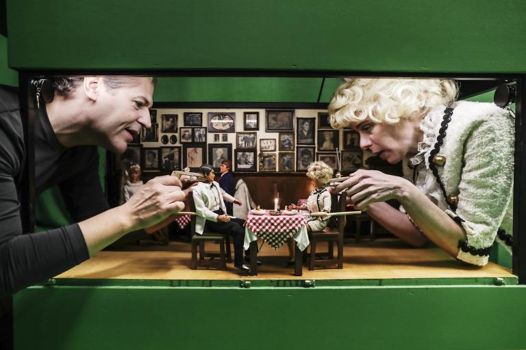 Två skådespelare med två dockor som sitter i en restaurangmiljö