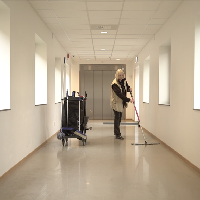 En äldre kvinna städar golvet i en korridor. 