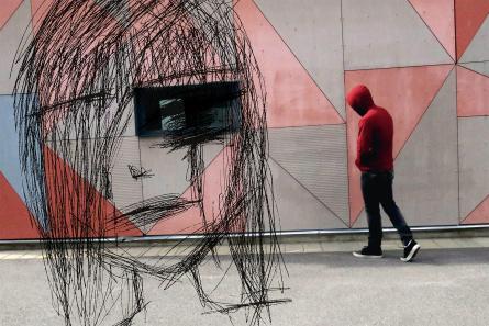 Tonåring med hoodie går förbi grafittivägg