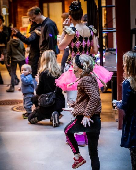 barn som dansar hoppsasteg, ballerina i bakgrunden tillsammans med andra familjer