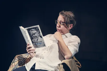 Kvinna sitter ner i en stol och läser en bok om Barbro Alving.