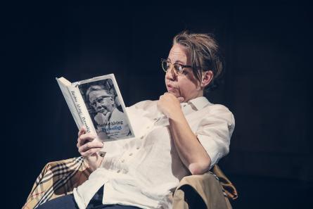 Kvinna sitter ner i en stol och läser en bok om Barbro Alving.