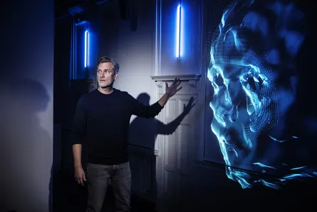 En person tittar på något utanför bild och pekar mot en digital projicering av ett ansikte