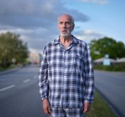 En äldre man står i pyjamas mitt i vägen och ser förbryllad ut.