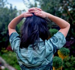 En person står i en trädgård med ryggen mot kameran, med händerna på huvudet