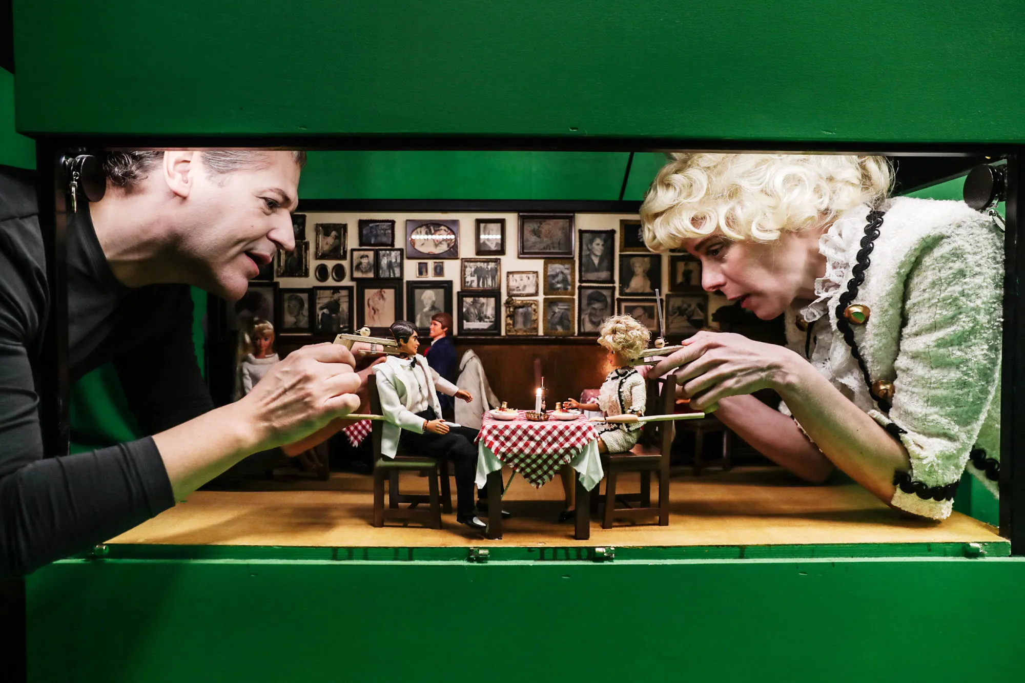 En person vid varje sida om ett dockhus. De spelar med barbiedockor.