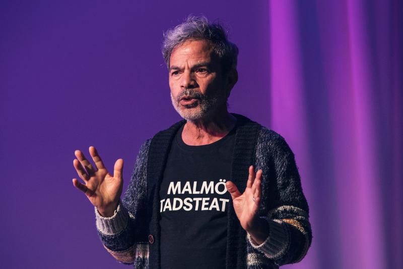 Person med Malmö Stadsteater-tröja står och pratar på en scen i lila ljus